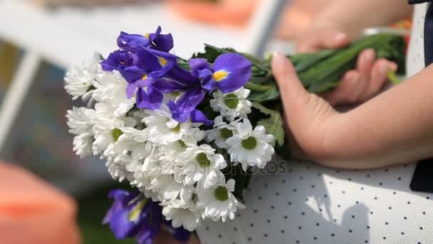 Vrouw houdt boeket van witte en blauwe veld bloemen op haar knieen — Stockvideo