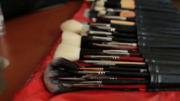 Pincéis de maquiagem jazem em suporte preto na mesa vermelha — Vídeo de Stock