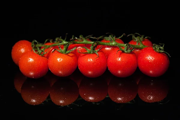 Colorful and fresh tomatoes with green stems and water drops on the black background — Stock Photo, Image