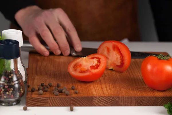Κοντινό πλάνο της αρσενική χέρι, ντομάτα σε ξύλο κοπής, με κοφτερό μαχαίρι — Φωτογραφία Αρχείου