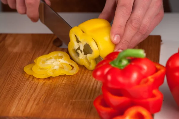 Large yellow and red sweet peppers cut into slices by chefs hands on woooden cutting board — Stock Photo, Image