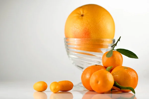 Sappige oranje in een glazen kom geplaatst op een whitbackground samen met enkele mandarijnen — Stockfoto