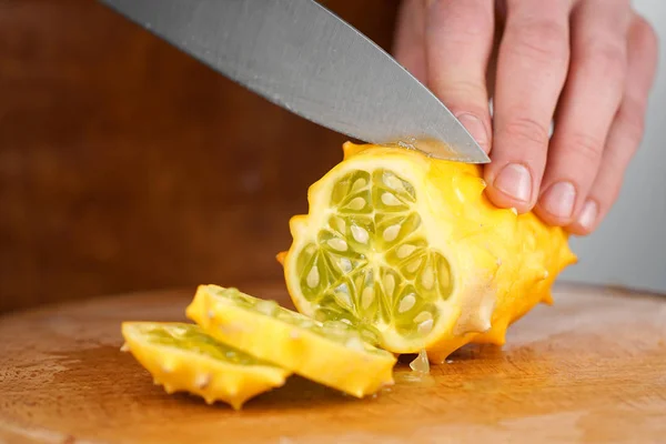 Primer plano de las manos de los chefs cortando melón kiwano en una tabla de cortar de madera — Foto de Stock