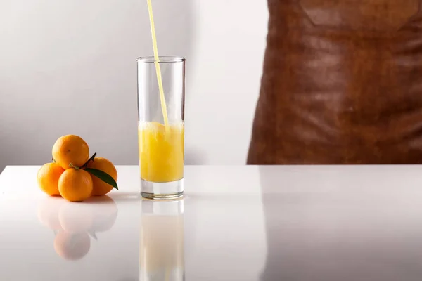Sumo de laranja derramando em vidro na superfície branca — Fotografia de Stock