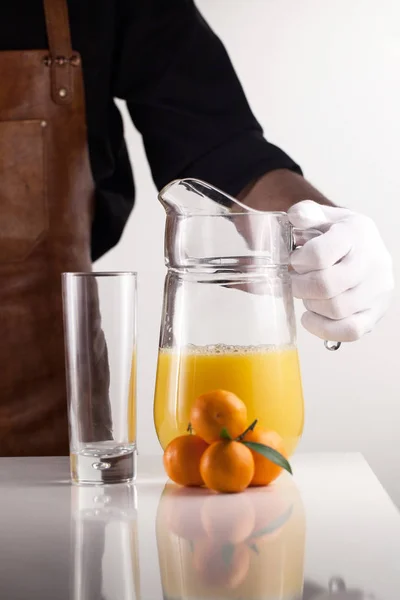 Koch hält ein Glas mit Orangensaft in der Hand. Komposition auf weißer Oberfläche — Stockfoto
