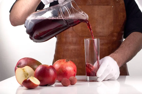 Man pouring juice into a glass. Composition of red fruits on a white background