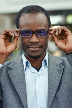 Gri takım elbise giymiş onun gözlük dokunmadan genç afroamerican adam