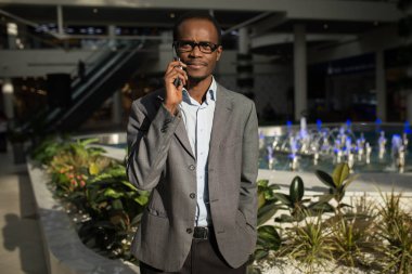Cep telefonu üzerinde konuşurken ve bir alışveriş merkezi dururken gülümseyen kendine güvenen genç Afrika adam.