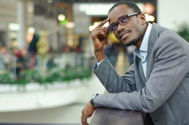 Küpeşte bir alışveriş merkezi yakınında duran dalgın afro Amerikalı adam.