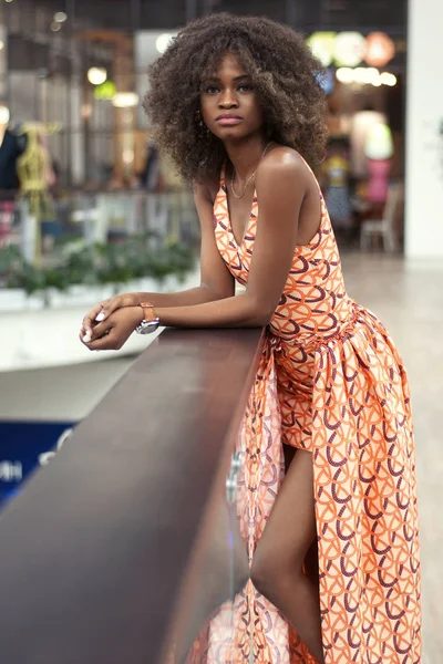 Gut aussehende junge afroamerikanische Mädchen in einem schönen langen Kleid steht in der Nähe von Geländer in einem Einkaufszentrum. — Stockfoto