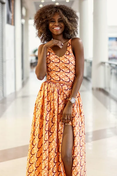 Lockiges afroamerikanisches Mädchen in einem langen Kleid steht in einem Einkaufszentrum. — Stockfoto