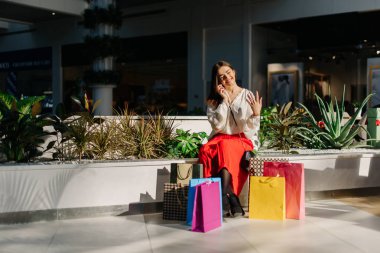Güzel kadın büyük Mall alışveriş sonra telefonla konuşurken bankta. Birçok alışveriş torbaları yakındır. Mutlu konuşma ve hareketleri eller erkek vardır.