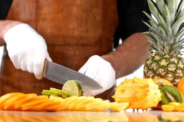 Chef rebanando lima en una tabla de cortar de madera entre otras frutas tropicales — Foto de Stock