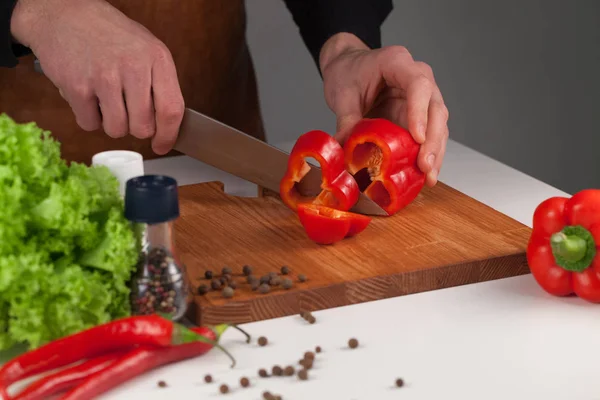 Man hands cut ripe red sweet pepper into thick pieses for salad