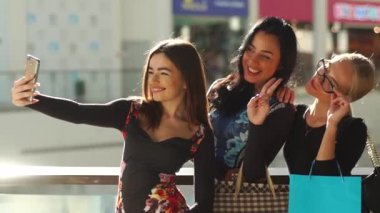 Çekici güzel kadınlar alışveriş sonra selfie alarak. Kızlar çok gülümseyen mutluyuz. Saç, yüz ve gözlük ellerine alarak fotoğraflar için poz. Birçok renkli alışveriş torbaları var.