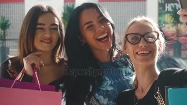 Çekici güzel kadınlar alışveriş sonra selfie alarak. Kızlar çok gülümseyen mutluyuz. Saç, yüz ve gözlük ellerine alarak fotoğraflar için poz. Birçok renkli alışveriş torbaları var.