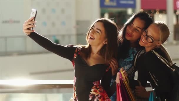 Charmed women taking selfie after shopping. Les filles sourient. Ils posent pour des photos, prenant leurs mains sur les cheveux, le visage et les lunettes. Avoir de nombreux sacs à provisions colorés . — Video