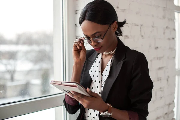 Menina muito afroamericana vestindo óculos e à procura de someting no tablet . — Fotografia de Stock