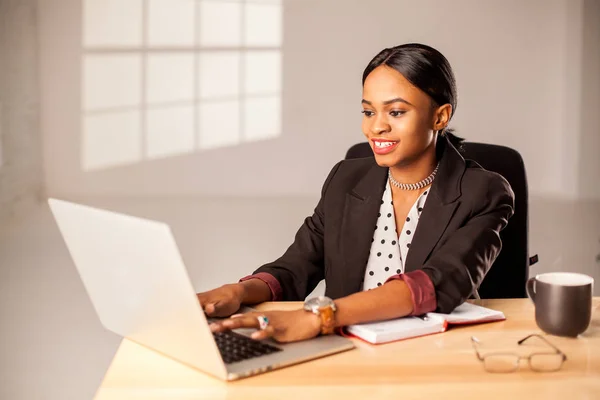 Sorriu afroamericana empresária trabalhando com seu laptop sentado no escritório . — Fotografia de Stock