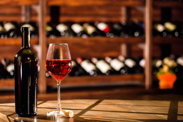 Composição de garrafa de vinho e copo de vinho. Prateleiras com garrafas de vinho no fundo . — Fotografia de Stock
