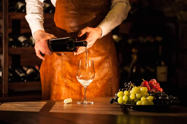 Sommelier versare il vino da una bottiglia in un bicchiere. Composizione di frutta e accessori per vino . — Foto Stock