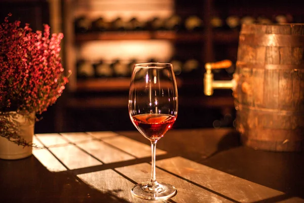Vino di vetro posto sul tavolo di legno accanto ai fiori e piccola botte di vino in legno . — Foto Stock