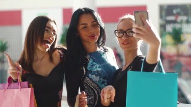 Çekici güzel kadınlar alışveriş sonra selfie alarak. Kızlar çok gülümseyen mutluyuz. Saç, yüz ve gözlük ellerine alarak fotoğraflar için poz. Birçok renkli alışveriş torbaları var.
