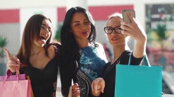 Çekici güzel kadınlar alışveriş sonra selfie alarak. Kızlar çok gülümseyen mutluyuz. Saç, yüz ve gözlük ellerine alarak fotoğraflar için poz. Birçok renkli alışveriş torbaları var. — Stok video