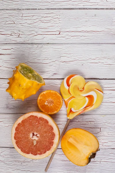 Vers fruit gesneden in helften en kleurrijke lolly. Samenstelling op een houten bord — Stockfoto