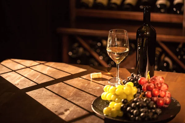 Composición en bóveda de vino. Copa y botella de vino junto al plato de frutas colocado sobre una mesa de madera . — Foto de Stock