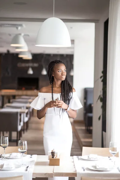 African american vrouw houdt van een glas wijn en permanent in de buurt van de geserveerd tafel in een restaurant. — Stockfoto