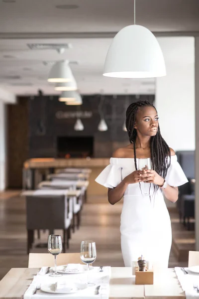 Aantrekkelijke afroamerican vrouw in een witte jurk poseren voor de camera met glas wijn in haar handen. — Stockfoto