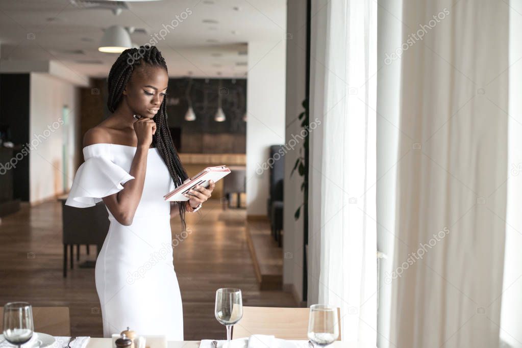 Attractive african american girl in beautiful white dress standing in the middle or the room.