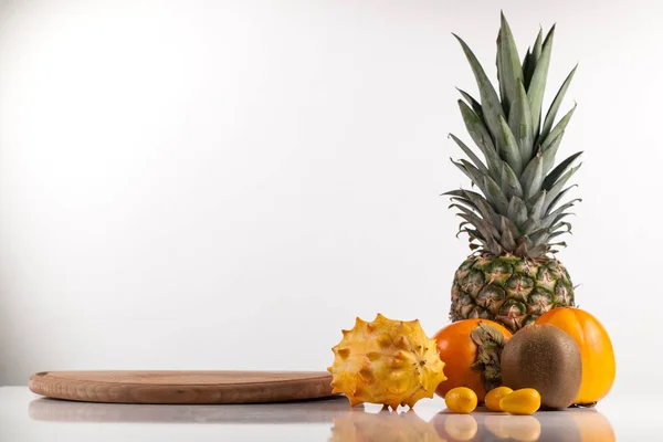 Frutos surtidos junto a un tablero de madera sobre una superficie blanca — Foto de Stock