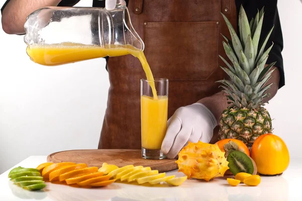 Erwachsene gießen einen Orangensaft in ein Glas aus einem Glas. Zusammensetzung einer reifen tropischen Frucht — Stockfoto