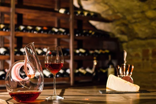 Caraffa di vino, bicchiere di vino e formaggio posti sul tavolo di legno in una volta di vino . — Foto Stock