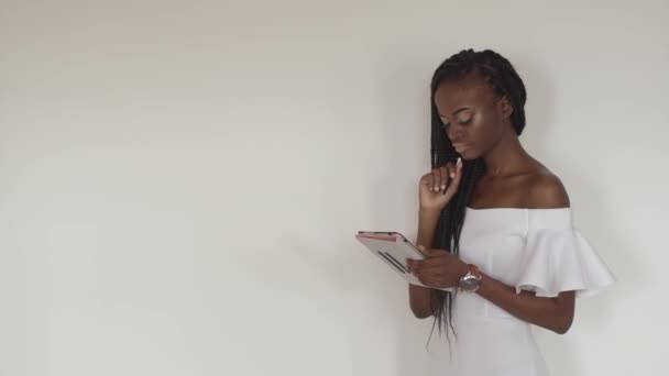 Το όμορφο το αφρο-αμερικανικό κορίτσι είναι κουβεντιάζοντας με τους φίλους της, χρησιμοποιώντας το tablet και φορώντας το λευκό elegent γυμνά ώμους φόρεμα. — Αρχείο Βίντεο