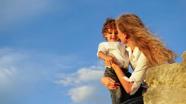 Güzel sarışın ling saçlı küçük kıvırcık oğlu sarılma. Gökyüzü arka plan üzerinde.