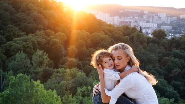 美しい若い母親は彼女の幼い息子を抱いてします。素敵な自然の風景. — ストック写真