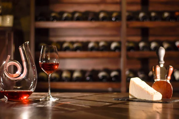Состав винного графина, бокала, сыра и аксессуаров на деревянном столе в винном погребе . — стоковое фото