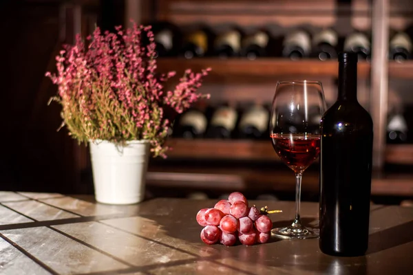 Set di bicchieri di vino, bottiglia, vaso di fiori e uva disposti su un tavolo di legno in una volta di vino . — Foto Stock
