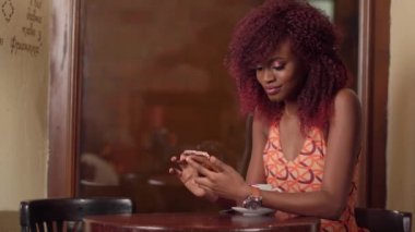 Güzel gülümseyen Afro-Amerikan kadın kısa kırmızı kıvırcık saçlı, manifatura arkadaşı vintage kafe penceresinde yakınındaki cep telefonu üzerinden yatay portresi