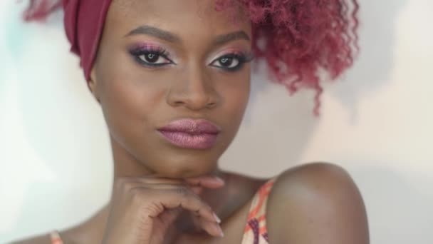 Οριζόντια γκρο πλαν πρόσωπο της γυναίκας αφροαμερικάνικης περιποιημένο με κόκκινα σγουρά μαλλιά και make-up κοντά στον λευκό τοίχο. Το βαθύ θέαμα από το όμορφο μοντέλο — Αρχείο Βίντεο