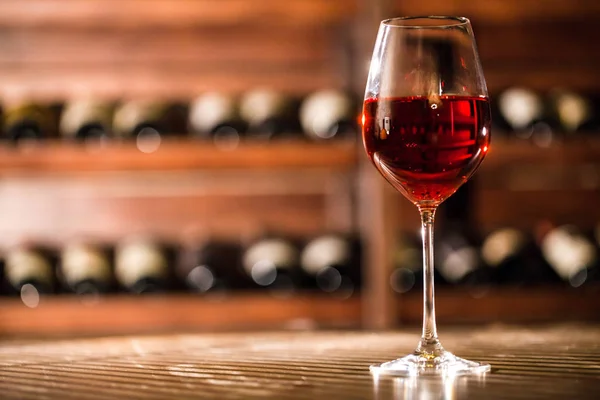 Wine glass with red wine in it placed on the table on the wine shelves background. — Stock Photo, Image