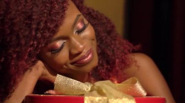 Gülümseyen Afro-Amerikan kadın kırmızı yuvarlak kutu altın şeritler yakınındaki kırmızı kıvırcık saçlı sevimli görme