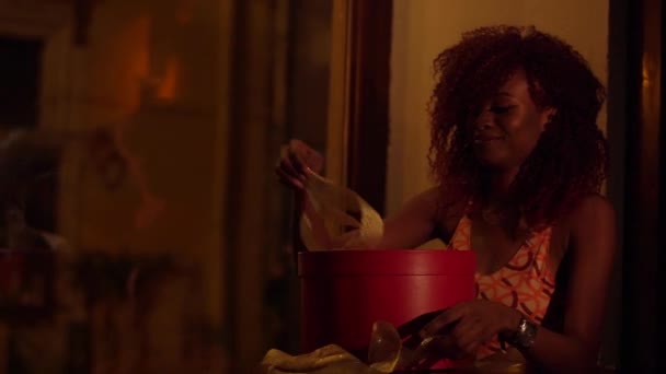 Il ritratto orizzontale della donna afro-americana sorpresa con i capelli ricci rossi sta aprendo il regalo di Natale in scatola rossa rotonda avvolta in nastri dorati nel caffè — Video Stock