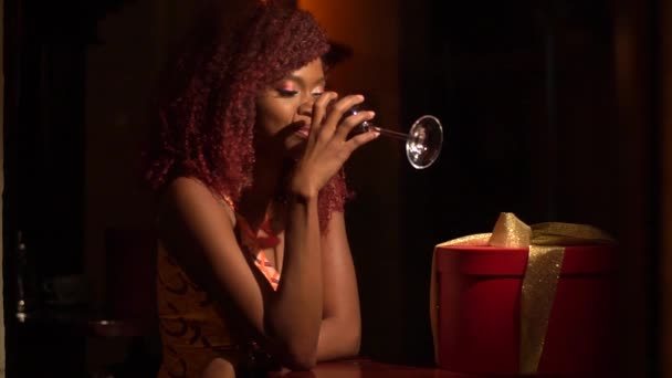 A visão profunda da menina afro-americana com cabelo encaracolado vermelho bebendo vinho no café escuro vintage sozinho — Vídeo de Stock