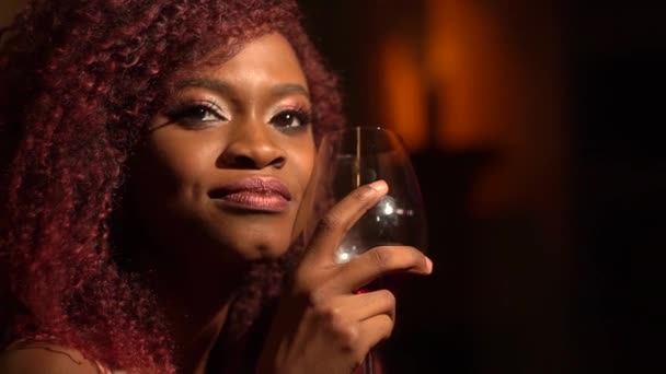 Portrét krásné afro-american ženy s hluboký a citlivý zrak a červenými kudrnatými vlasy těší její červené víno a víno v kavárně — Stock video