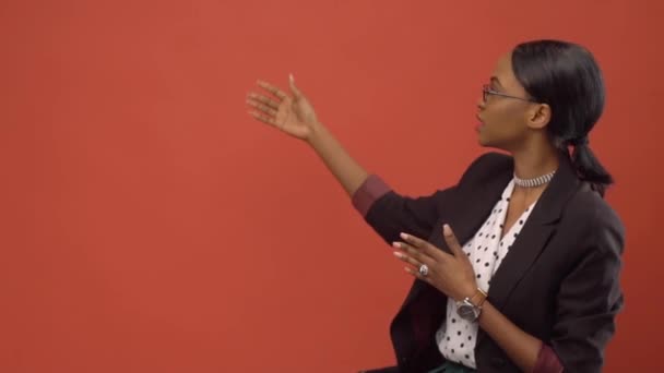 Черная женщина поднимает руки, говоря о чем-то перед стеной. — стоковое видео