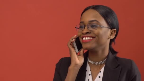 Alegre bonita senhora fala no seu iPhone antes de vermelho parede — Vídeo de Stock